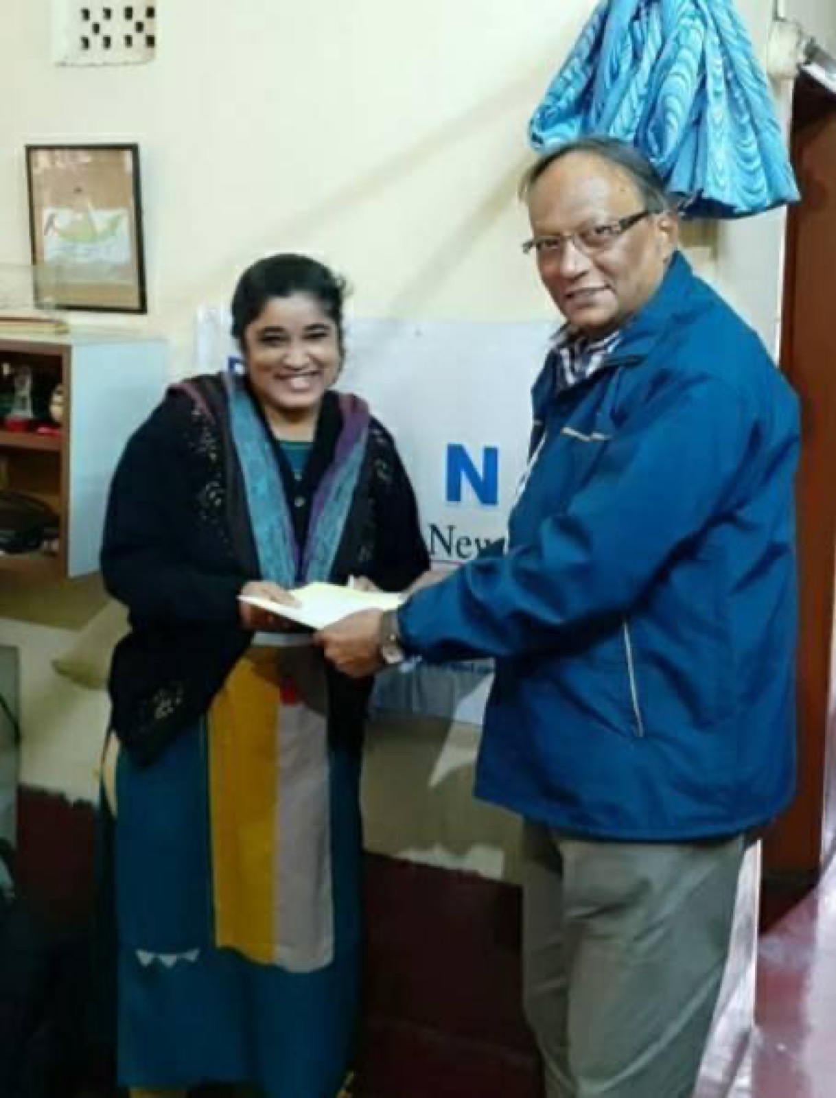 A DAND supporter hands a First Step grant to a woman in the DAND office.