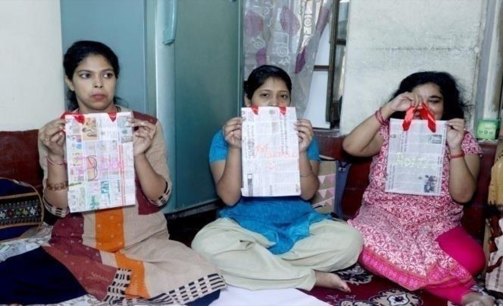 Three women at a DAND workshop hold up the paper bags they made.